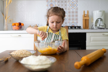 serious child helping in kitchen. kid cooking food. little cute girl in apron in preparing dough, baking pie, cookies, making biscuit.