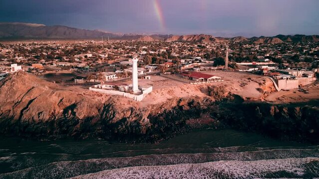 revealing aerial view of San Felipe's lighthouse at the coast, beach with waves and rainbow, Video a&eacute;reo del faro de San Felipe, Baja California, M&eacute;xico 