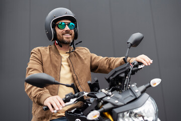 Obraz na płótnie Canvas Bearded brutal biker wearing helmet and stylish sunglasses preparing riding motorbike