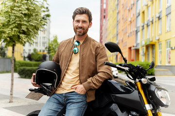 Smiling man biker holding helmet and looking at camera on sport motorcycle