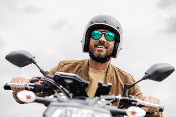Handsome bearded brutal biker wearing helmet and stylish sunglasses riding motorbike