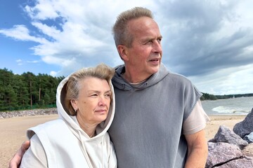 Portrait of happy elderly senior couple in love walking on a beach at summer, smile, laugh, have fun 
