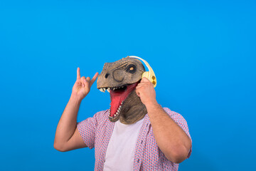 Fototapeta premium funny man with a dinosaur head listens to music in my headphones on a blue isolated background