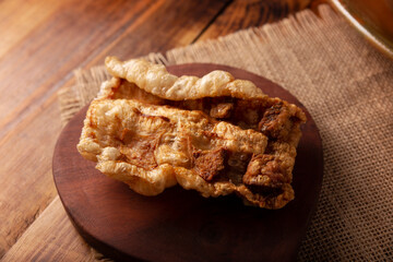 Chicharron. Crispy Fried pork rind, are pieces of aired and fried pork skin, traditional Mexican ingredient or snack served on wooden cutting board
