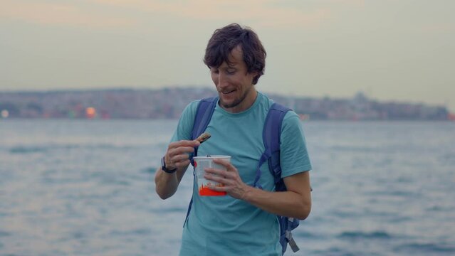 A bearded man is portrayed in on a pier, relishing a mouthwatering traditional Turkish dish of mussels with rice. The camera captures the delectable meal, showcasing the flavors and textures of this