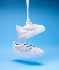 Contemporary white perforated shoes hanging on shoelaces on a gradient blue background. Close up....