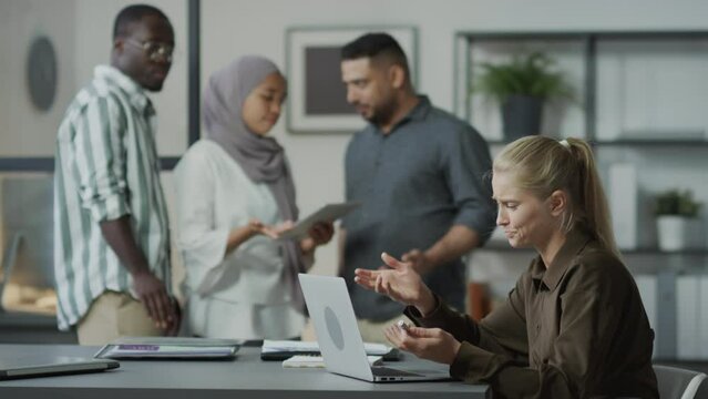 Selective focus shot of stressed Caucasian woman working on laptop in office feeling humiliated when envious co-workers slandering her