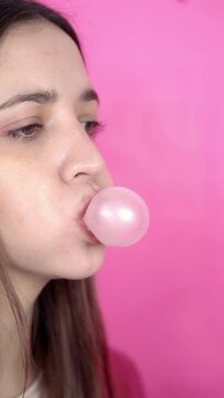 Young brunette woman making bubblegum baloons on pink background