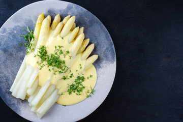 White asparagus glazed with sauce hollandaise and cress served as top view on a design plate with...