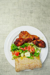 Cooked meal on a plate with marinated chicken drumsticks and fresh salad and Italian bread. Mediterranean style food. Selective focus. High quality product. Healthy eating.