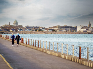 Two women walking on a Mutton island causeway. Galway city in the background. Popular town landmark...