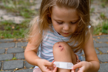 A little girl accident and plaster with a band aid on the knee of boy with an injury, wound or...