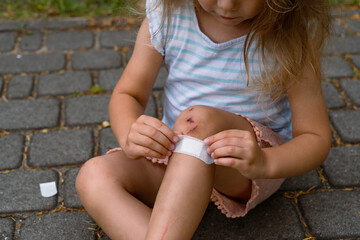 A little girl puts a band-aid on a wound on her knee after an accident. Selective focus.