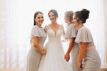 Fototapeta premium Portrait of the bride with her friends. The bride is posing in a voluminous white dress and her beautiful friends in gray evening dresses. Brunettes Open shoulders. Morning of the bride.