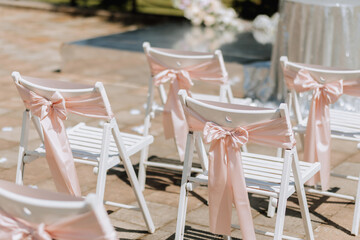 Wedding ceremony in the yard. Round arch made of flowers and many white chairs with pink ribbons....