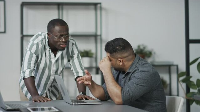 African American manager telling offensive words to his Middle Eastern subordinate at work in officeAfrican American manager telling offensive words to his Middle Eastern subordinate at work in office