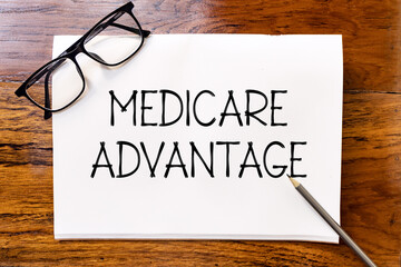 Medicare advantage handwriting text on blank notebook paper on wooden table with pencil and glasses...