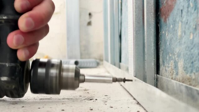 Installation of a frame for drywall indoors. The worker fixes the elements of the metal structure with screws. Close-up