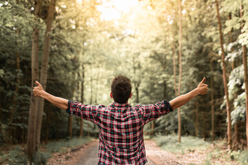 Fototapeta na wymiar Young man in autumn forest raising arms, expressing carefree happiness and connection with nature.