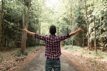 Rear view of young man feeling joyful with arms raised in autumn forest