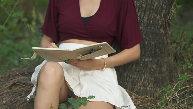 Young woman in a white skirt reading a book by a palm tree