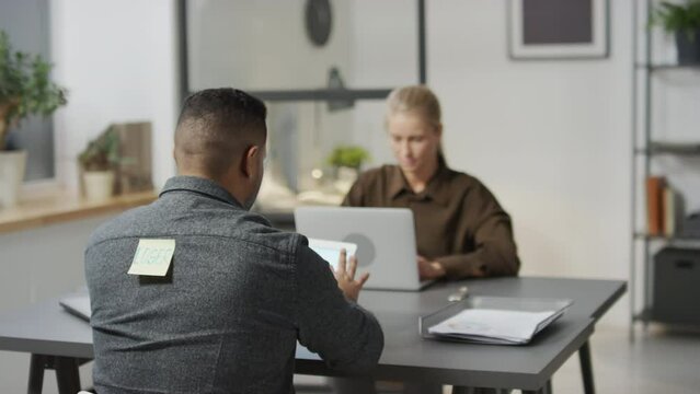 Selective focus shot of African American bully sticking paper with offensive word on his colleagues back