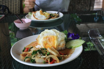 Fried egg with basil and sea food in thai style on table