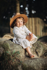 Little girl wearing hat, sitting bootless in the countryside