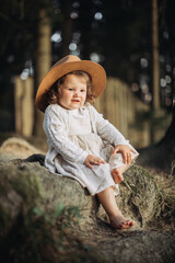 Little girl wearing hat, sitting bootless in the countryside