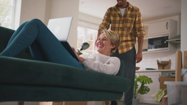 Young couple at home relaxing on sofa in lounge making video call on laptop on moving day - shot in slow motion