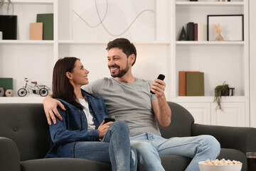 Happy couple spending time together at home. Man changing TV channels with remote control