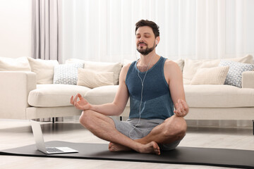 Man in sportswear meditating near laptop at home. Harmony and zen - obrazy, fototapety, plakaty