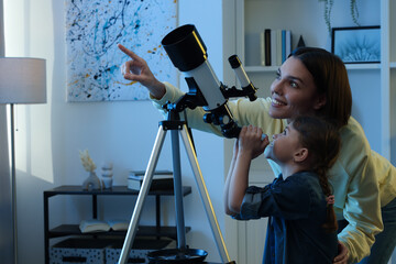 Happy mother and her cute daughter using telescope to look at stars in room