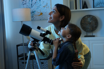 Happy mother and her cute daughter using telescope to look at stars in room