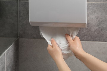Woman taking new fresh paper towel from dispenser in bathroom, closeup
