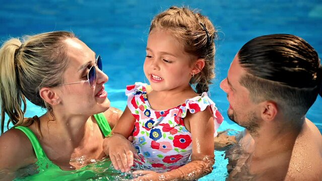 Happy parents kissing their smiling daughter while swimming in the pool. Slow motion