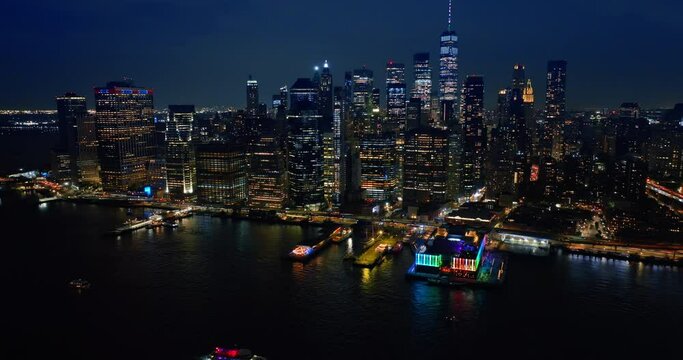 Approaching one of the multiple piers of New York with neon illumination from above the river. Amazing skyscrapers skyline at backdrop.