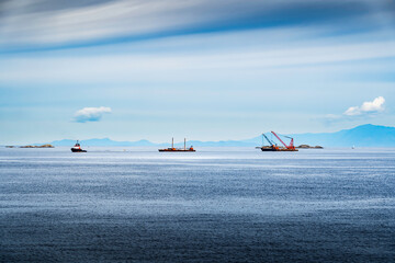 A tug boat pulling pile driving equipment on barges while passing through the Gulf Islands and Strait of Georgia near Nanaimo British Columbia Canada.