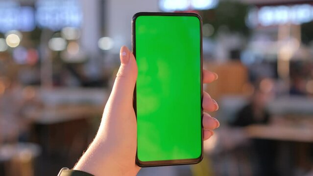 Handheld Camera: back view of brunette holding chroma key green screen smartphone watching content. Shopping online. Gadgets and contemporary people concept.