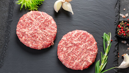 Fresh raw meat burger cutlet on the black slate board with herbs and spices for background. Copy...