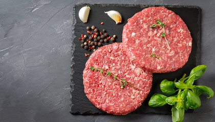 Fresh raw meat burger cutlet on the black slate board with herbs and spices for background. Copy space, top view . - obrazy, fototapety, plakaty