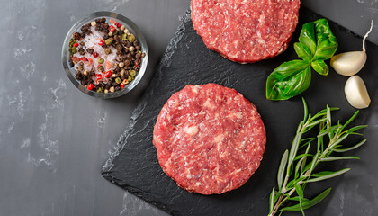 Fresh raw meat burger cutlet on the black slate board with herbs and spices for background. Copy...