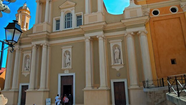 Tourists visit Basilique Saint-Michel Archange de Menton. People taking pictures of the colored buildings in Menton, French Riviera.