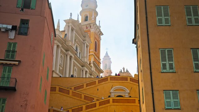 Tourists visit Basilique Saint-Michel Archange de Menton. People taking pictures of the colored buildings in Menton, French Riviera.