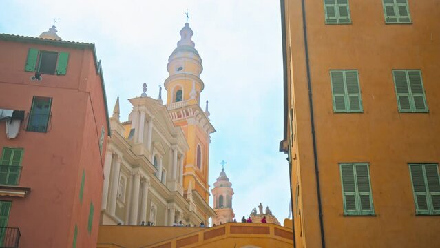Tourists visit Basilique Saint-Michel Archange de Menton. People taking pictures of the colored buildings in Menton, French Riviera.