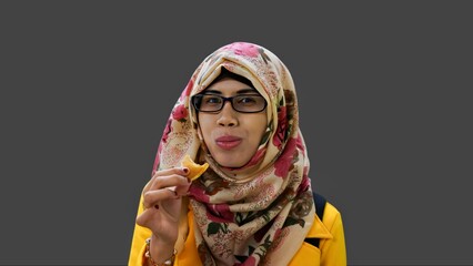 Close up portrait of smiling young Muslim woman wearing yellow jacket and brown hijab with red flower motif holding and eating small brown cake.