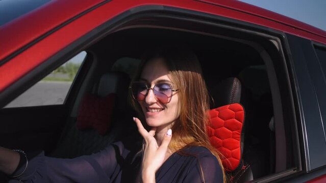 Close-up of a beautiful girl sitting behind the wheel in a red car during the day in the light of the sun. Dancing and singing
