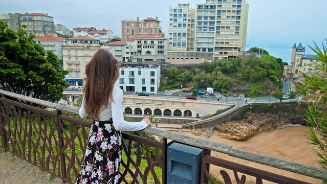 Beautiful girl approaching the edge overlooking elegant seaside town Biarritz. A model woman looking and exploring European royalty resort town in the south of France, Basque coast.