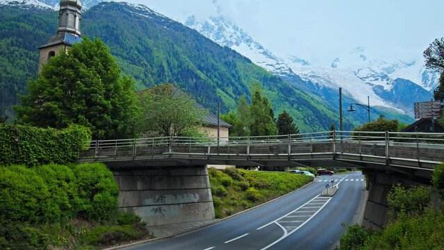Old French Church and a bridge over the road with Alps mountains in Chamonix. Scenic view of Chamonix-Mont-Blanc during summer with snow on the peak of the mountains in France