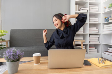 Cute asian woman listening to music happily on her laptop and enjoying listening to music at home.